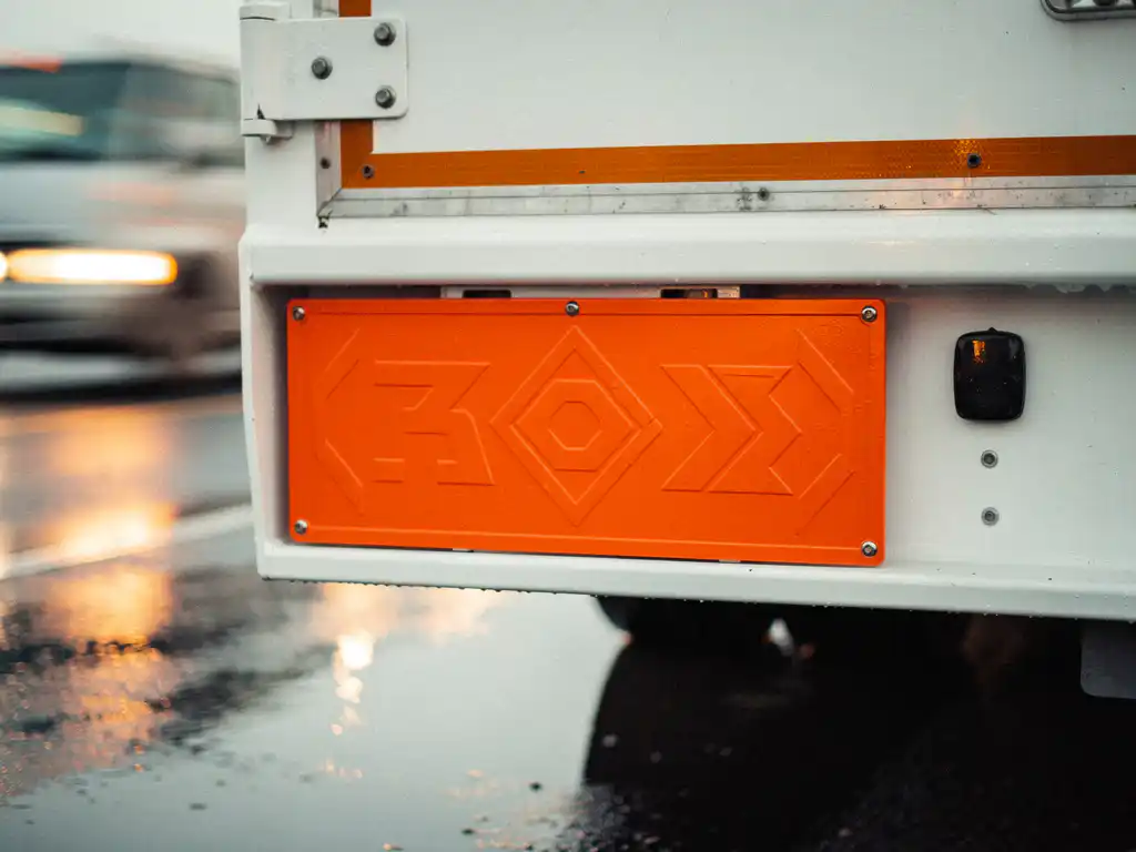 Oranje gevarenidentificatiebord met nummercode op de achterkant van een witte vrachtwagen op een natte snelweg.